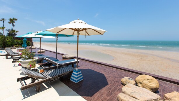 Eine Strandterrasse mit Liegestühlen, Sonnenschirmen und Blick auf den Ozean.