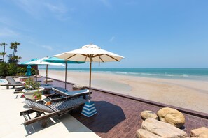 A beachside patio with lounge chairs, umbrellas, and a view of the ocean. - My Resort Beach Apartment (Hua Hin)
