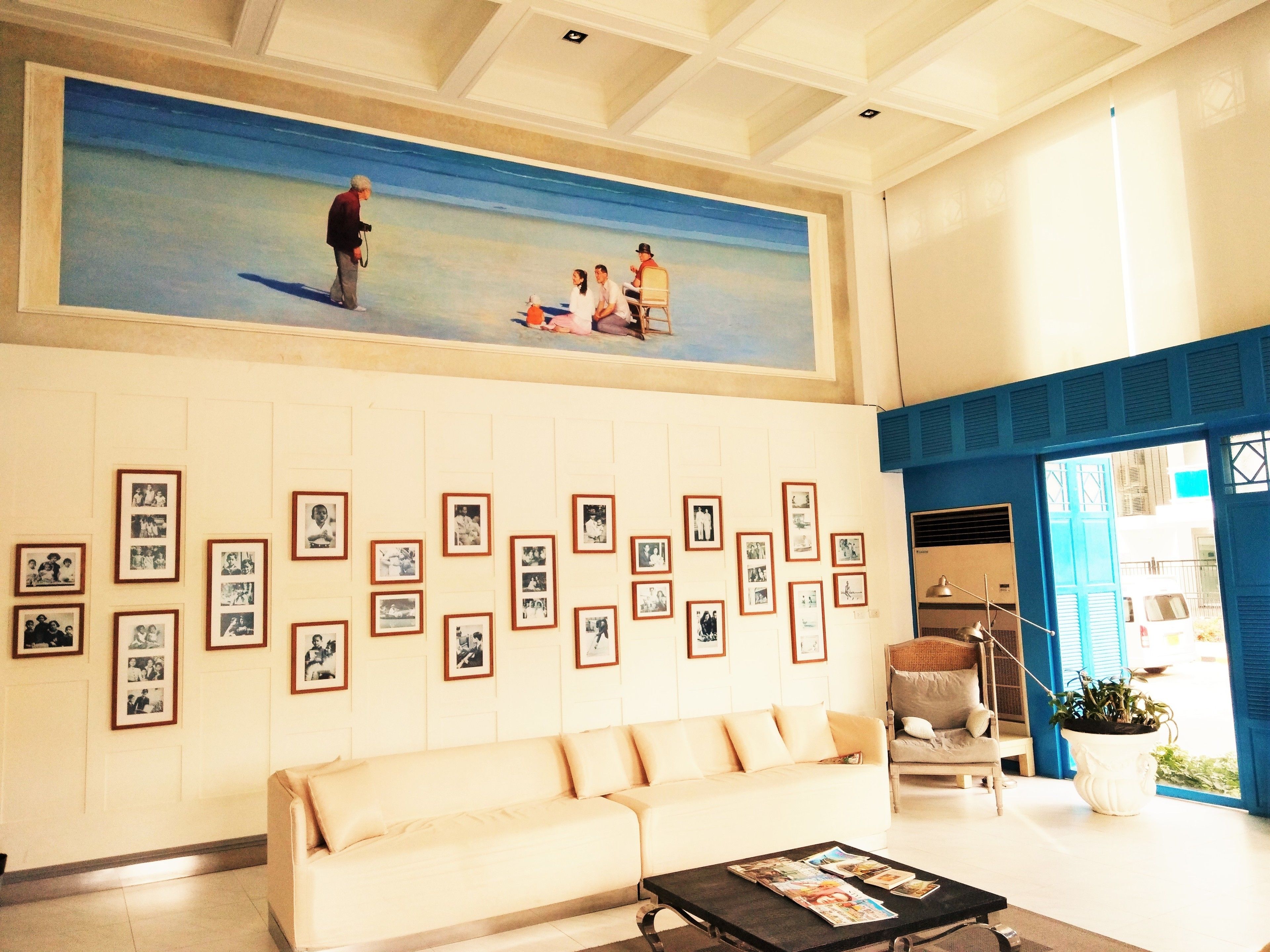 Eine Empfangshalle mit einem großen Gemälde einer Strandansicht, einer Reihe gerahmter Fotografien an der Wand, einem beigefarbenen Sofa und einem Couchtisch mit Zeitschriften.
