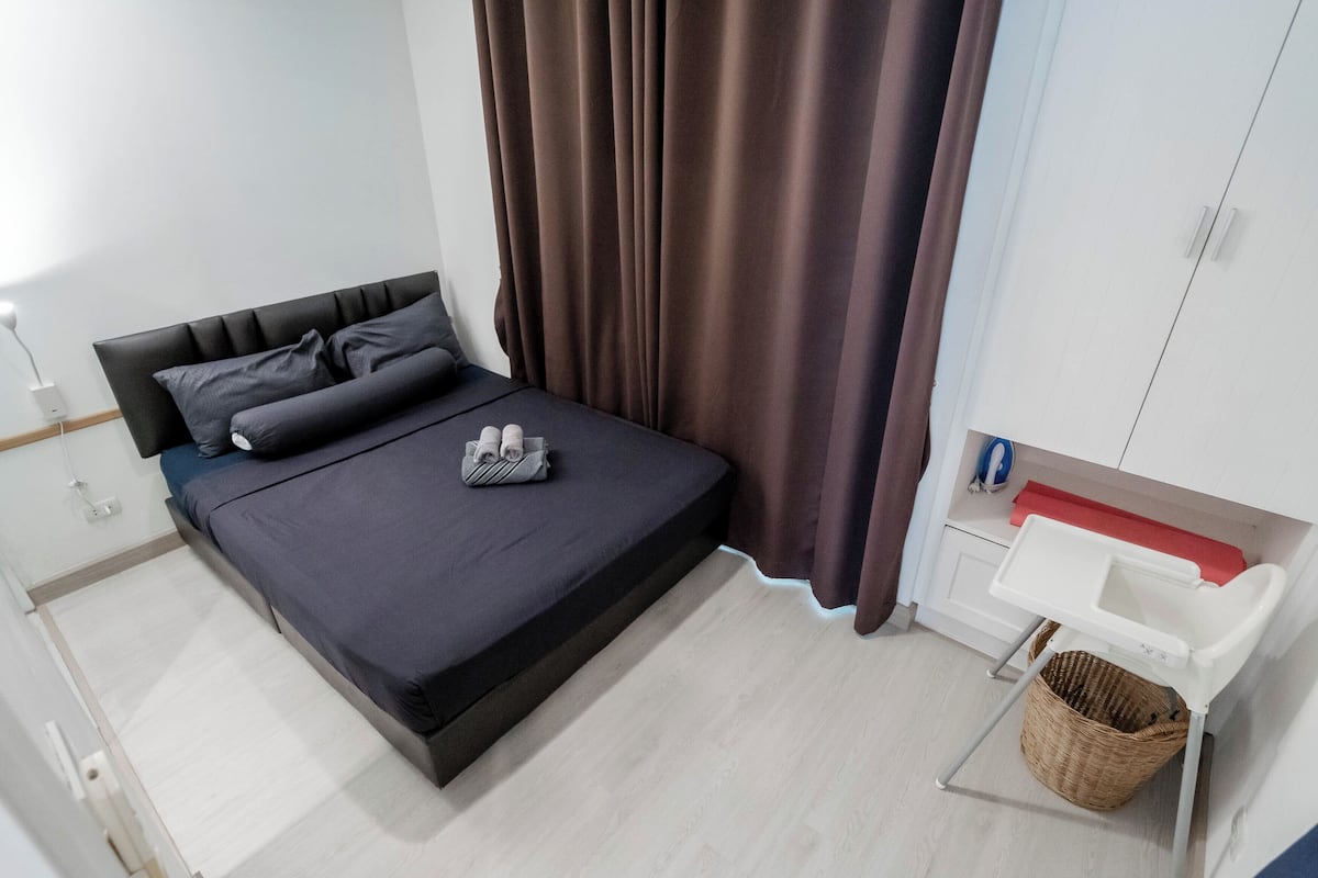 Une chambre à coucher avec un lit, une table de chevet, une petite armoire blanche et un panier en osier.
