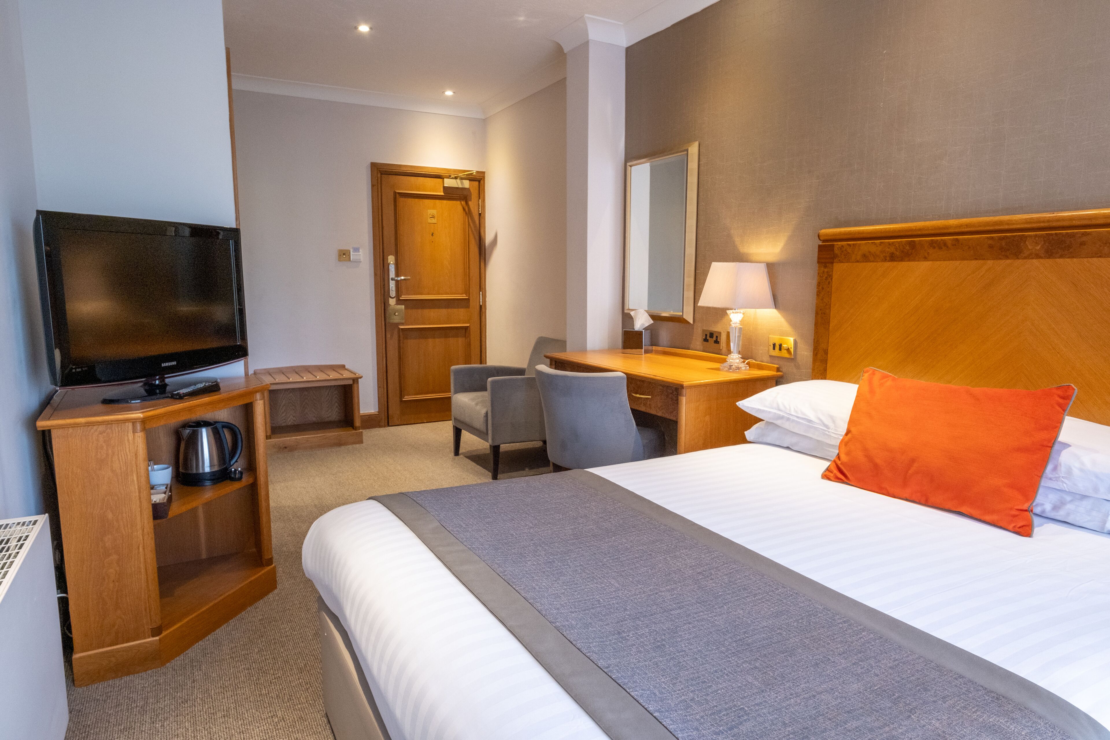 Een hotelkamer met een bed, een bureau met stoel, een televisie en een houten kast.