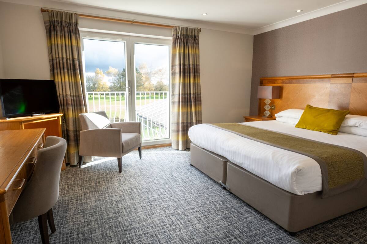 A hotel room with a bed, a desk, a chair, a television, and a balcony with curtains.