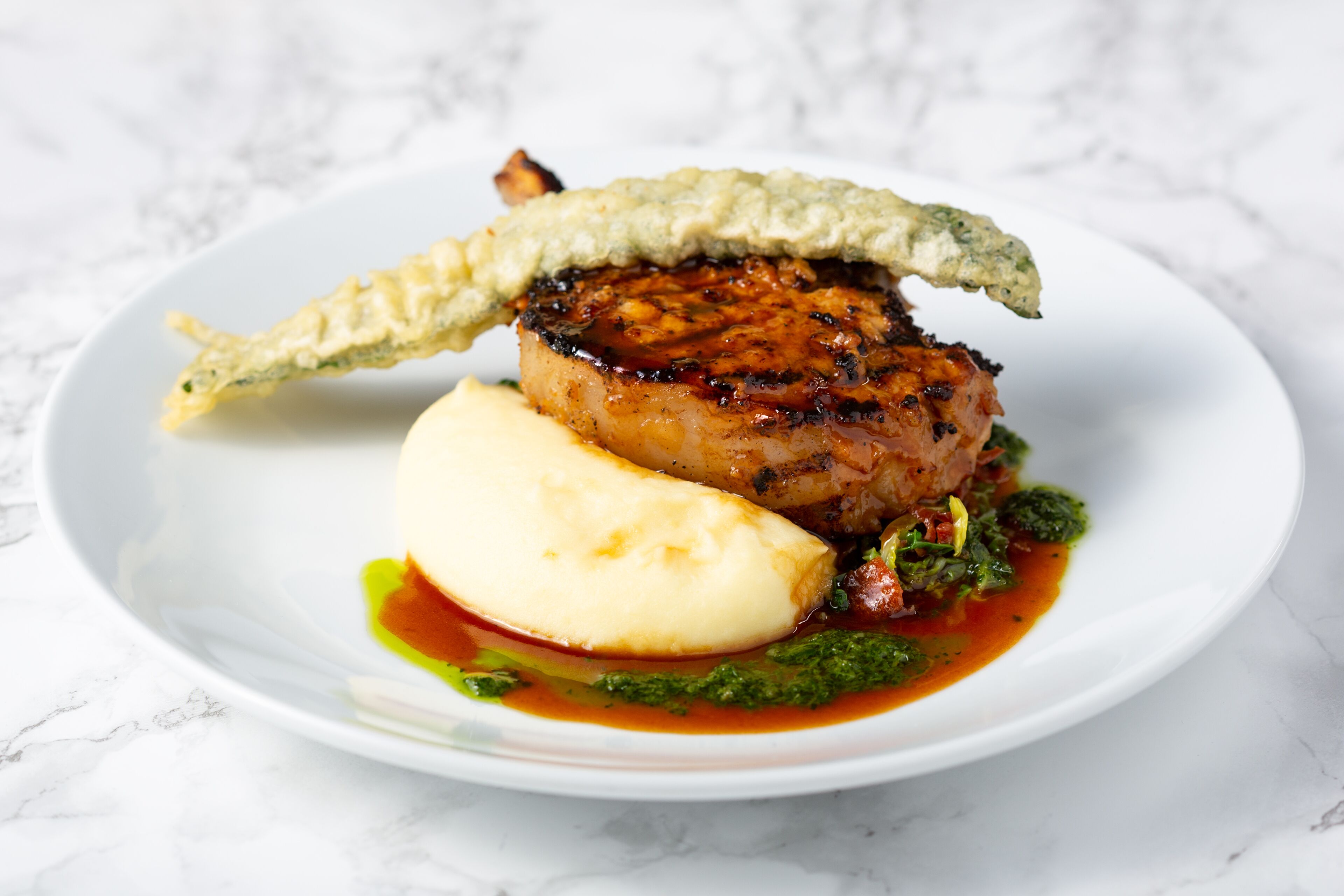Ein Teller Essen mit Fleisch, Kartoffelpüree und grüner Soße.