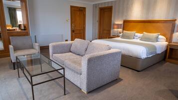 Una habitación de hotel con una cama grande, un sofá, una mesa de centro de vidrio y puertas de madera.