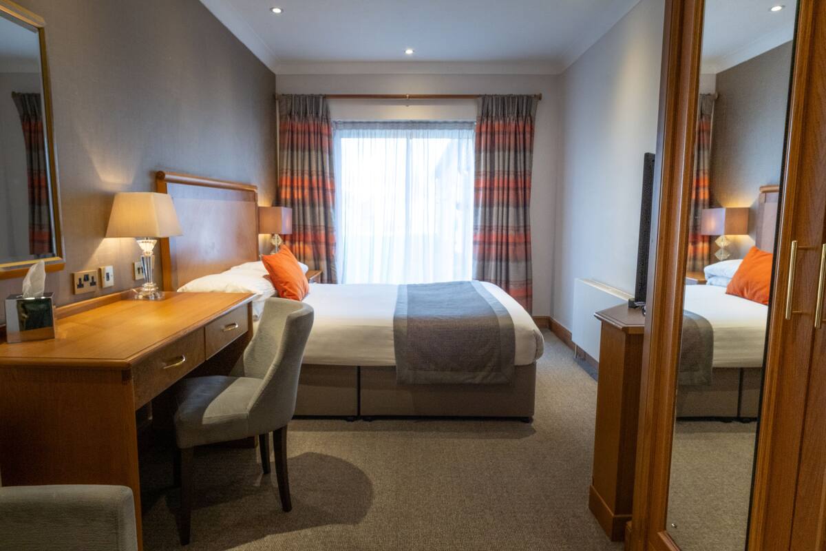 A hotel room with a bed, a desk, a chair, a mirror, and a window with curtains.
