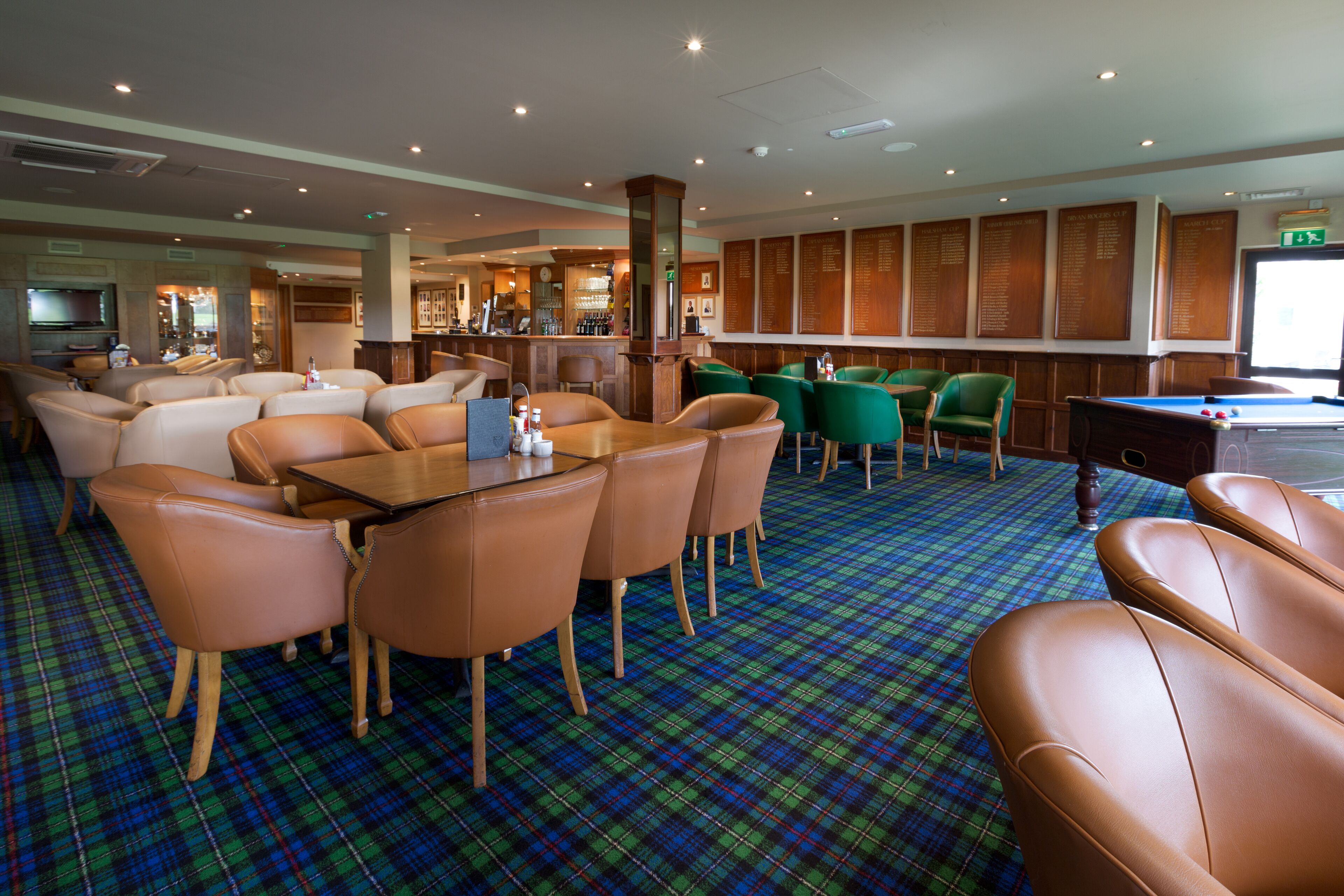 A hotel lobby with a pool table, leather chairs, a bar area, and a blue plaid carpet.