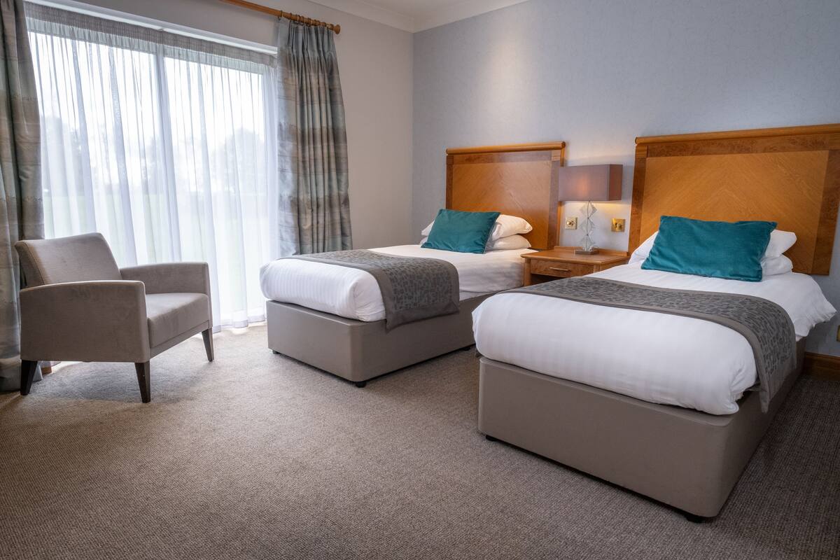 A hotel room with two beds, a chair, and a nightstand.
