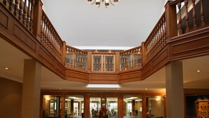 Un lobby espacioso con una imponente escalera, un candelabro y una zona de estar central con un tapete estampado.