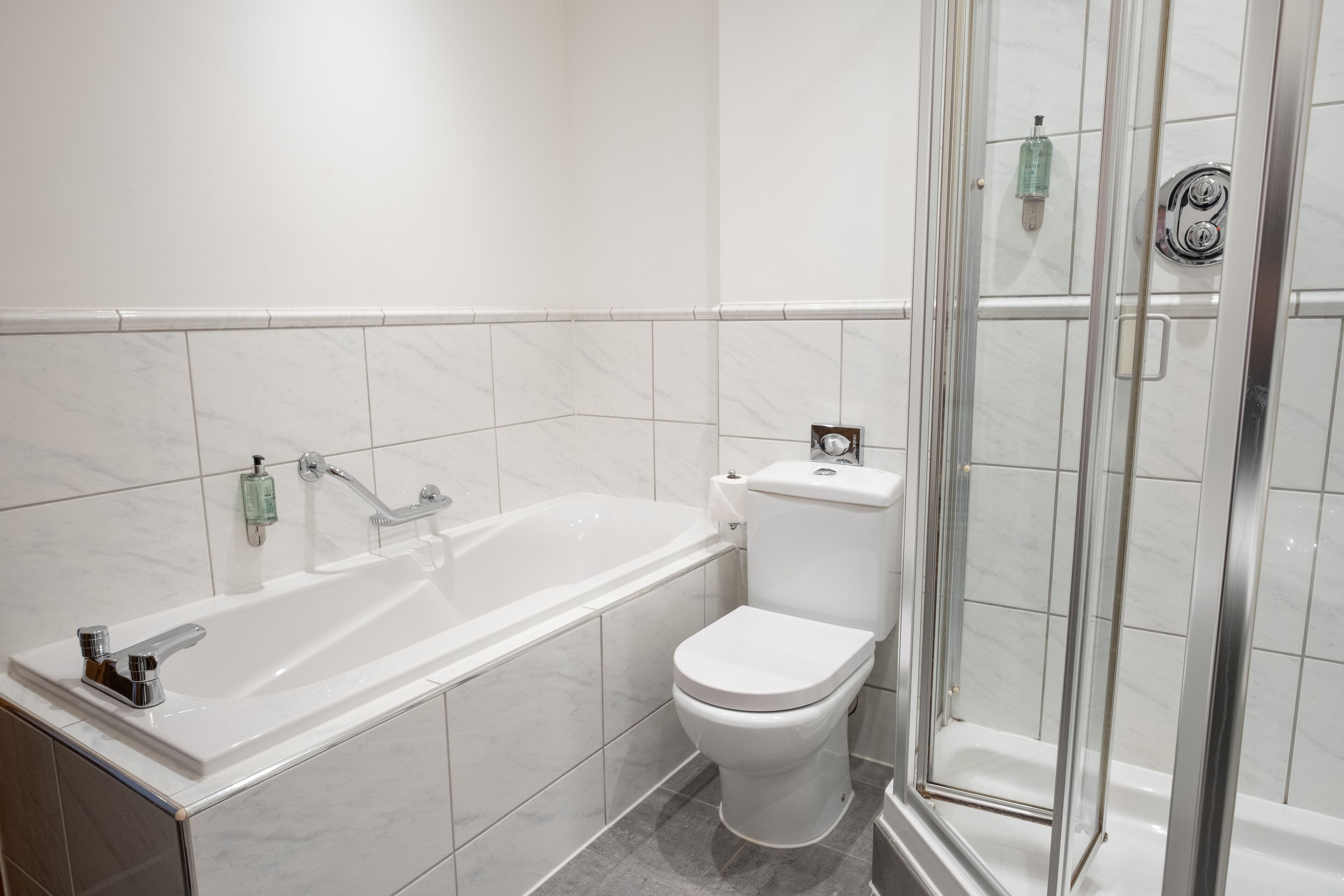A modern bathroom with a bathtub, toilet, and glass-enclosed shower.