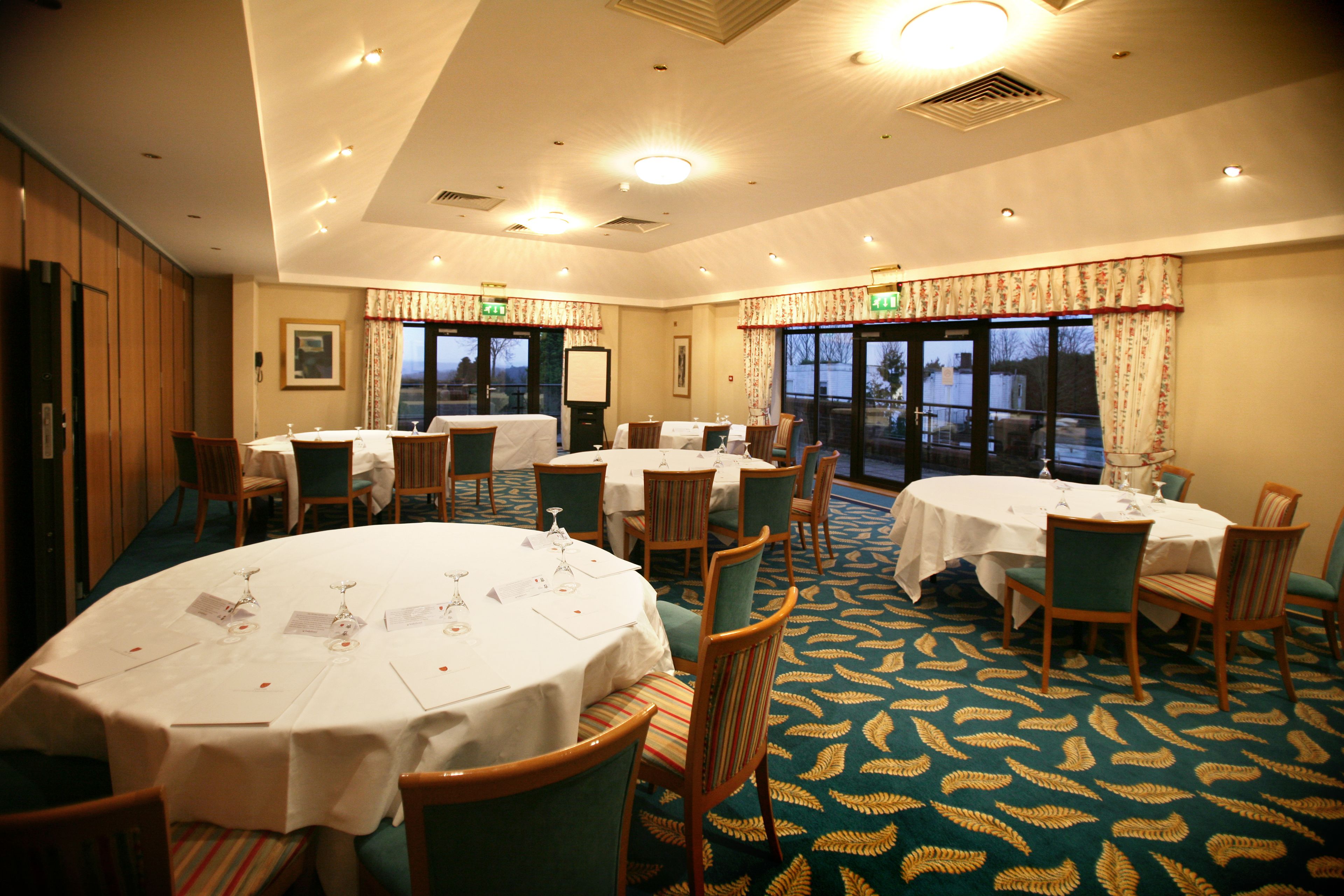 A conference room with multiple round tables, chairs, and a carpeted floor.