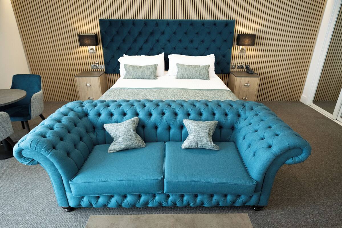 A hotel room with a large bed, a tufted blue sofa, a small table, and two nightstands with lamps.
