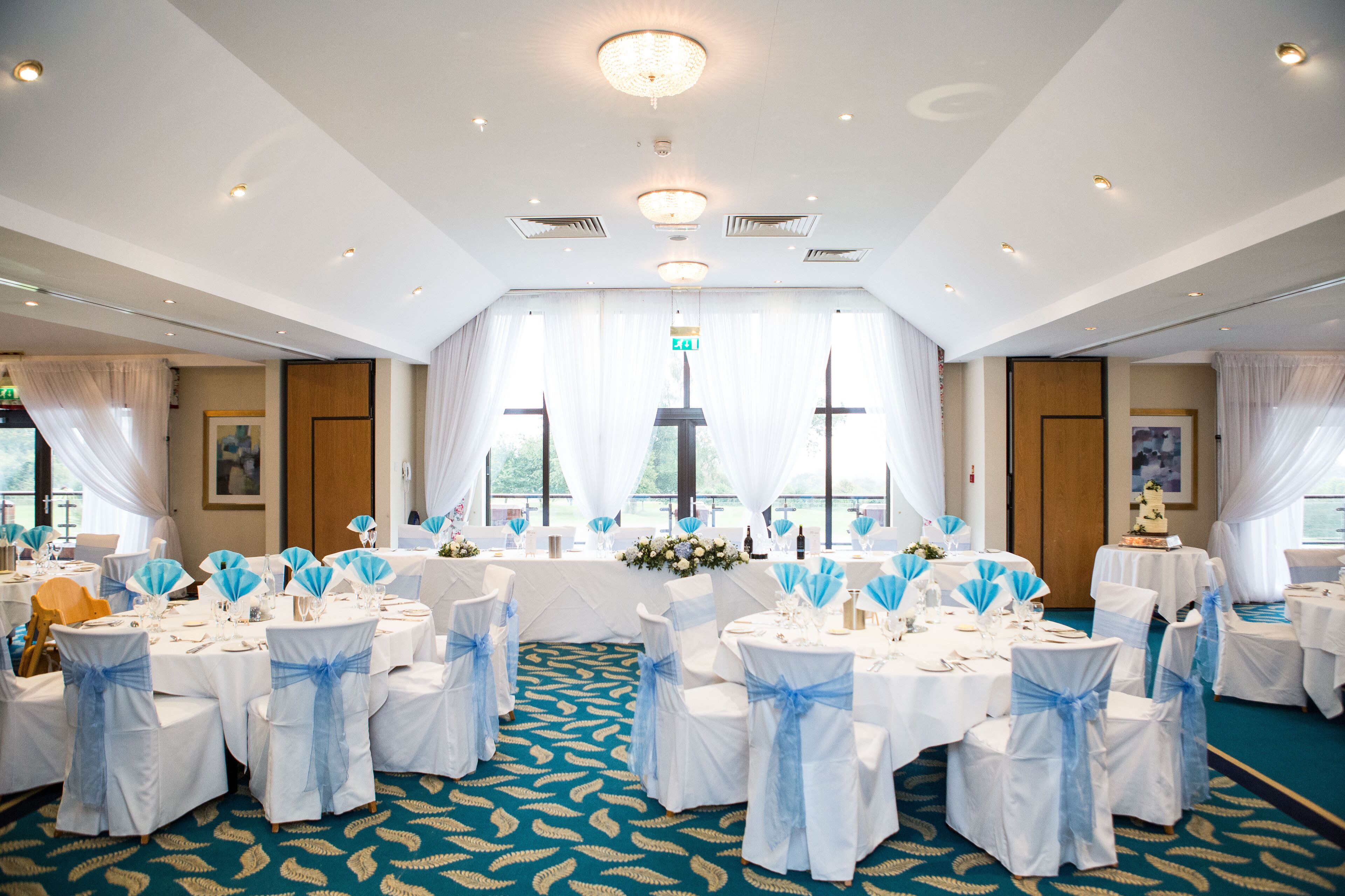 A banquet hall with round tables, white tablecloths, and blue chair sashes.