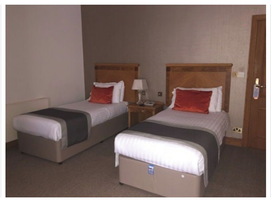Two single beds with wooden headboards, a nightstand with a lamp, and a door with a lock.