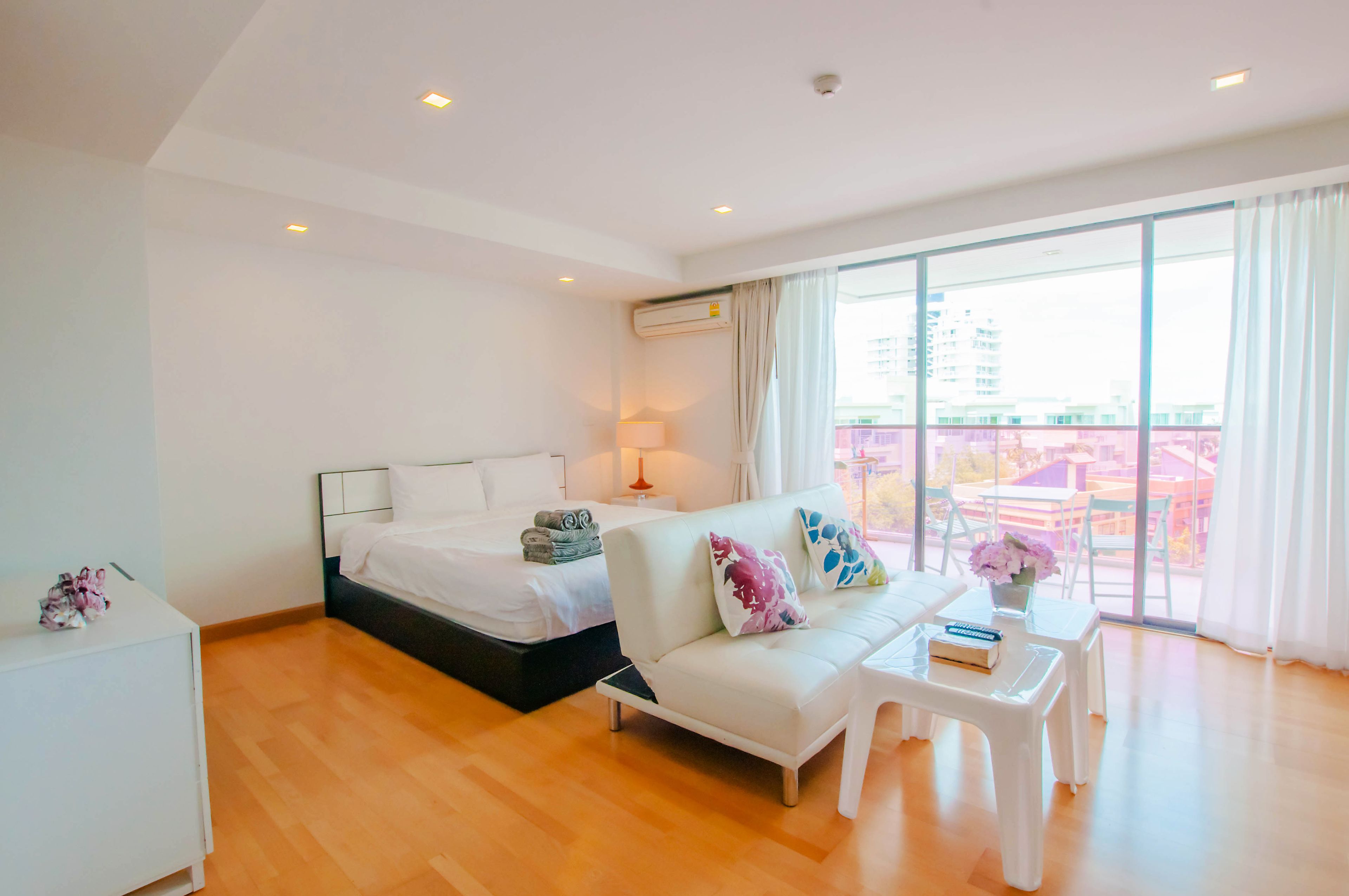 A modern hotel room with a bed, a sofa, a small table, and a balcony with a view.