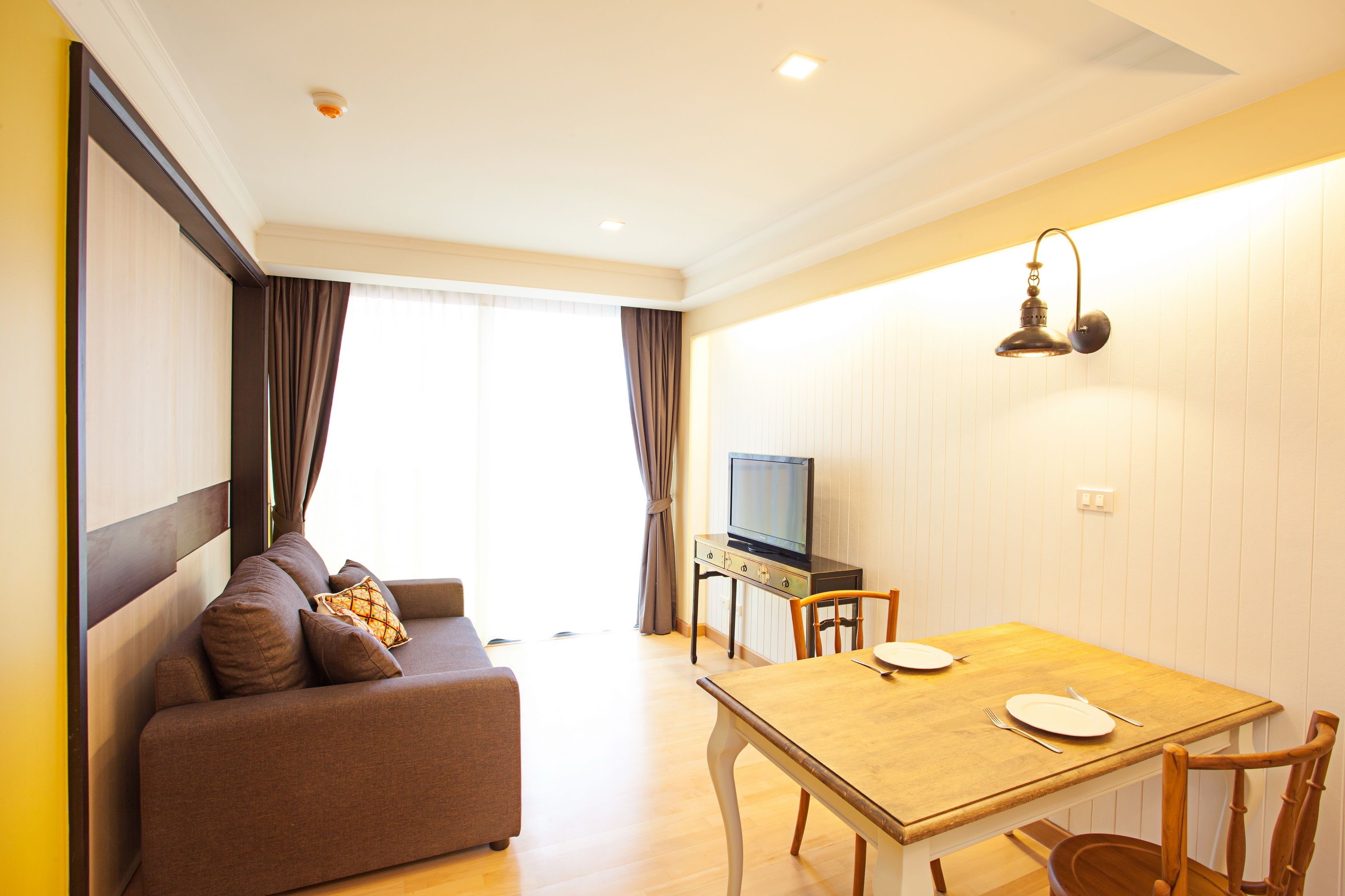 A modern living room with a sofa, a dining table with chairs, a television, and a wall-mounted light fixture.