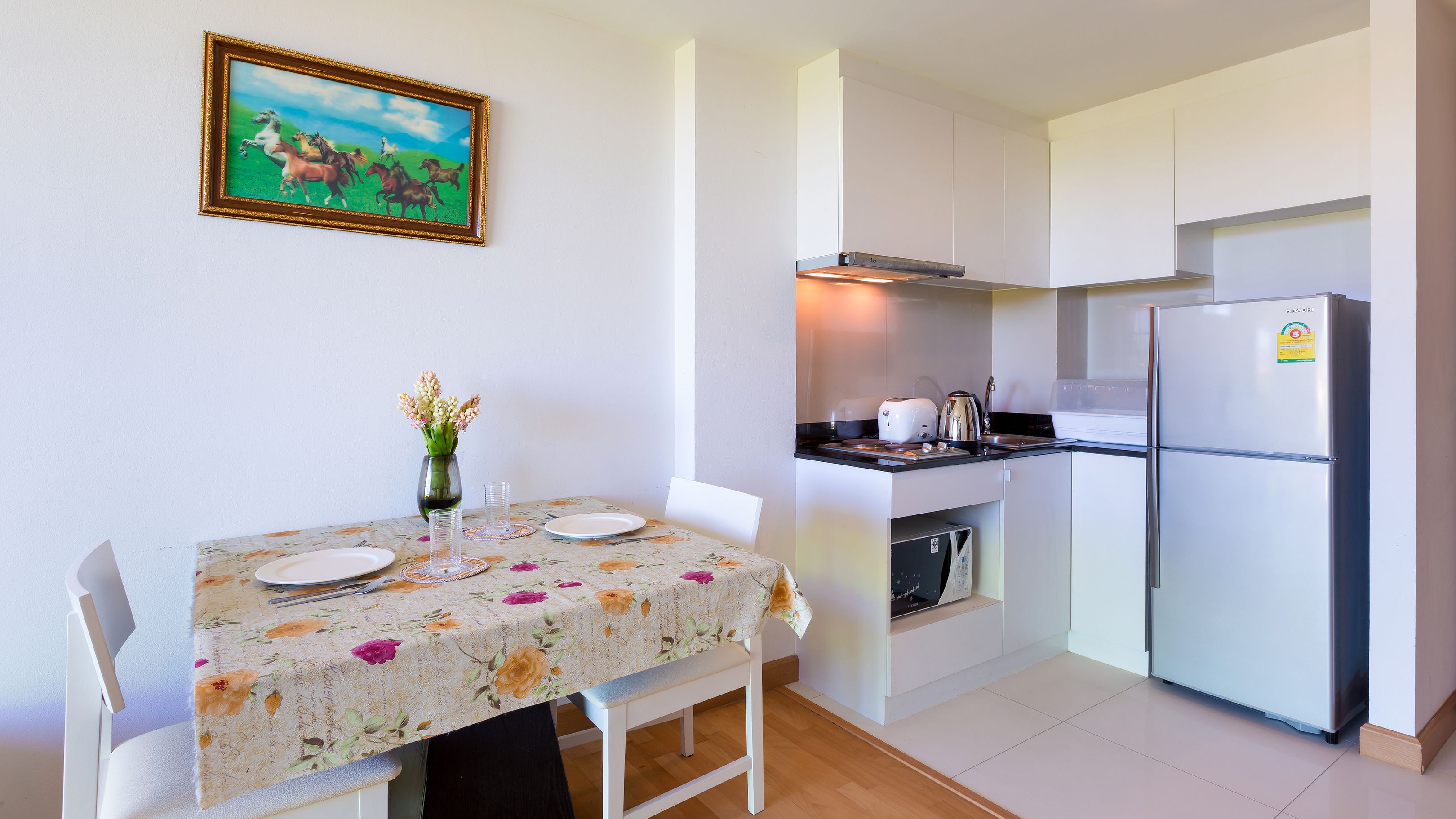 A compact kitchen with a refrigerator, stove, and sink. There is a dining table with chairs and a vase of flowers.