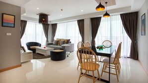 A modern living room with a dining area, large windows with curtains, a sofa, a coffee table, and a dining table with chairs. - Rocco Hua Hin Beach Seaview (Hua Hin)