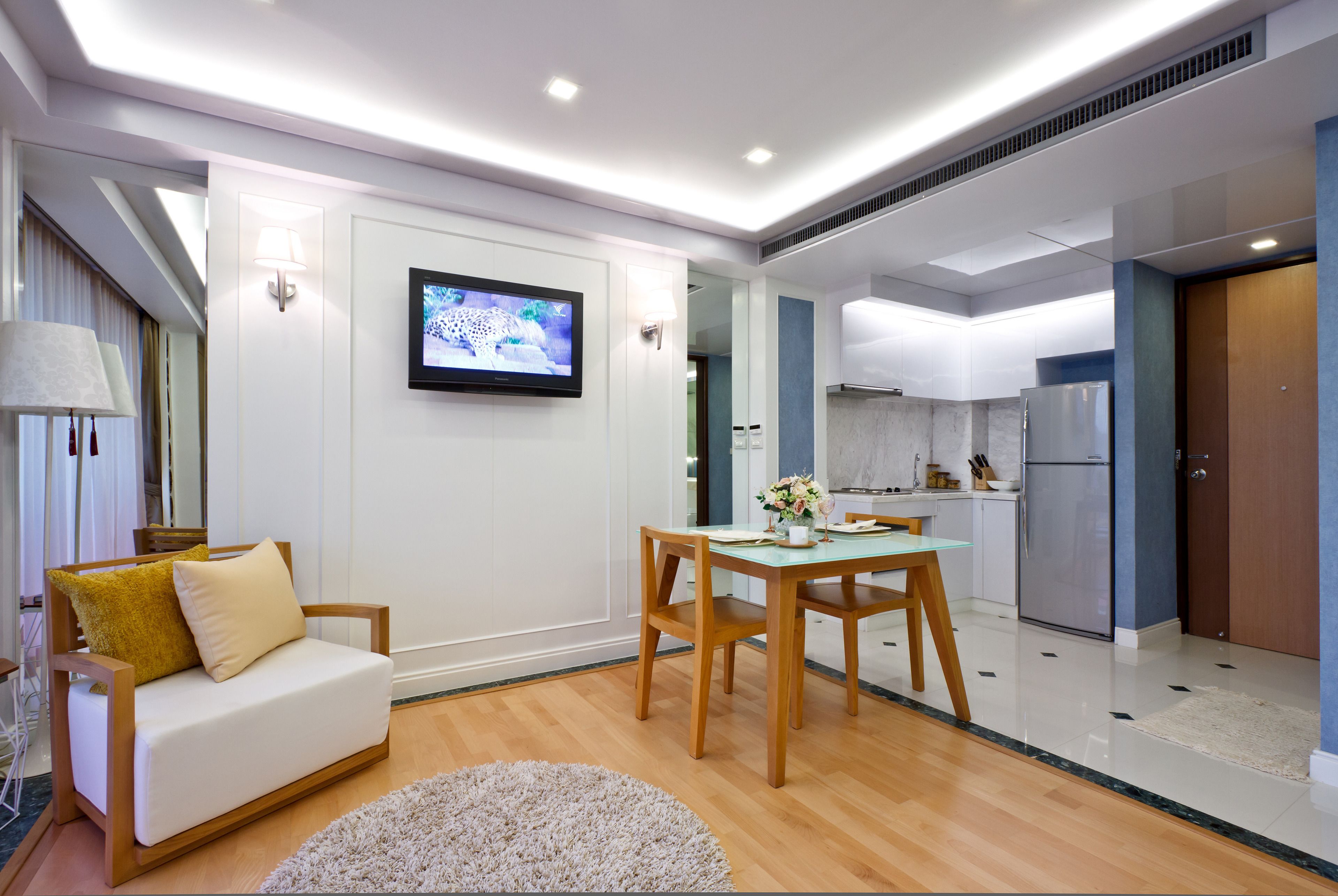 A modern living room with a sofa, a dining table, and a TV mounted on the wall.