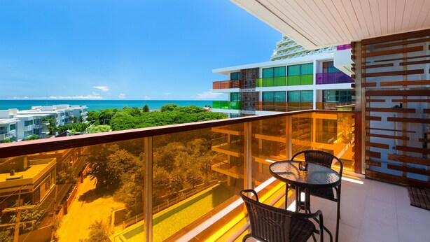 A balcony with a view of the sea, a dining area with chairs, and a building with multiple balconies. - Rocco Hua Hin Beach Seaview (Hua Hin)