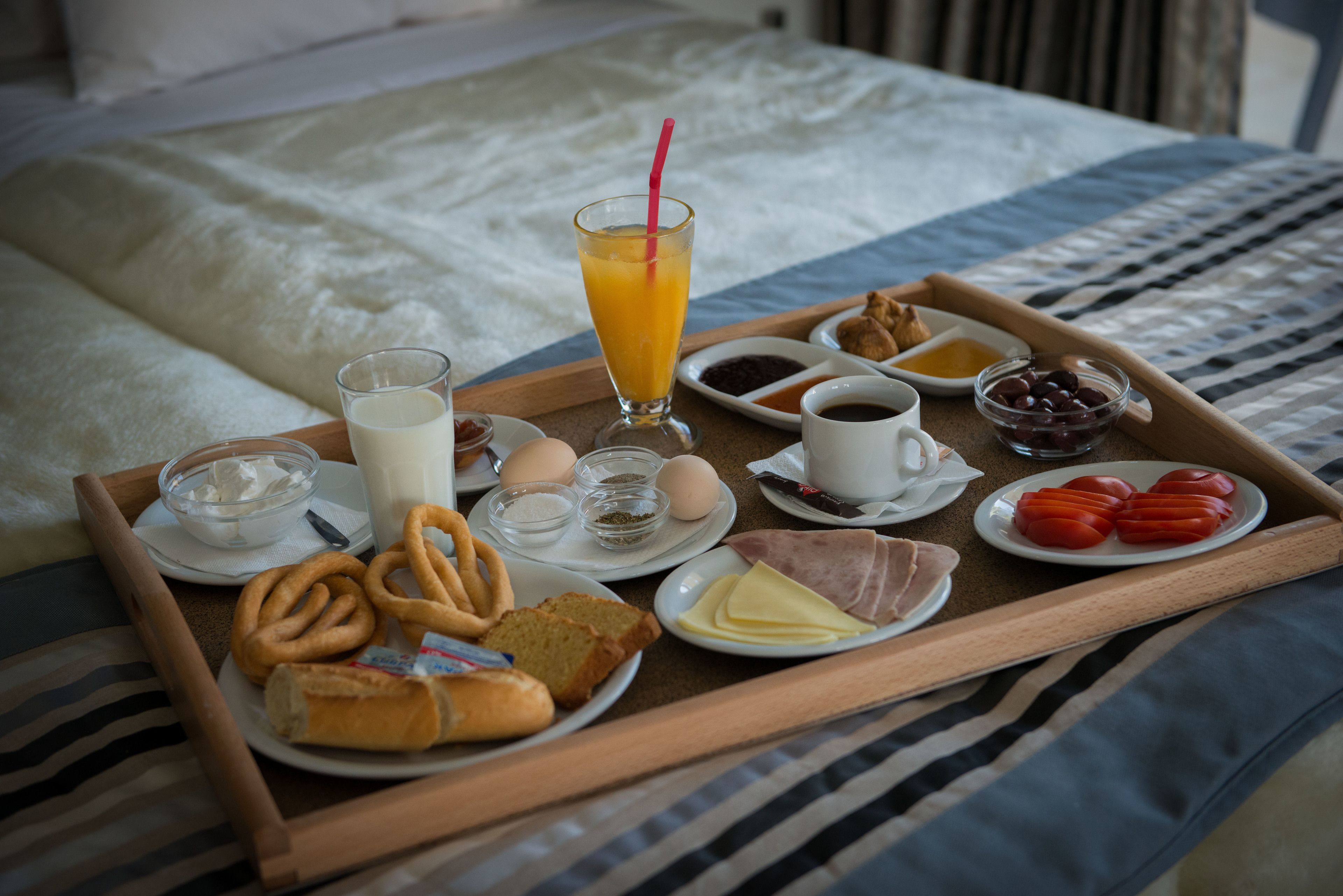 A breakfast tray with various foods and drinks on a bed.