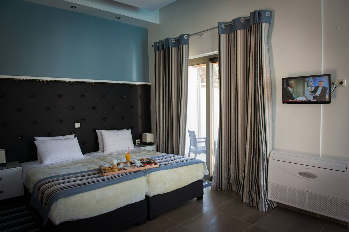 A hotel room with a large bed, a flat-screen TV, and a balcony with curtains.