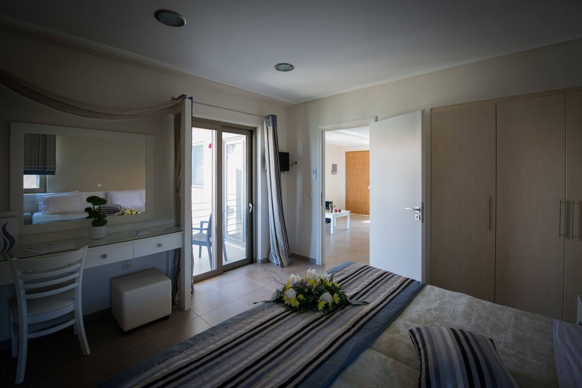 A hotel room with a bed, a desk with a chair, a wardrobe, and a bathroom visible through an open door.