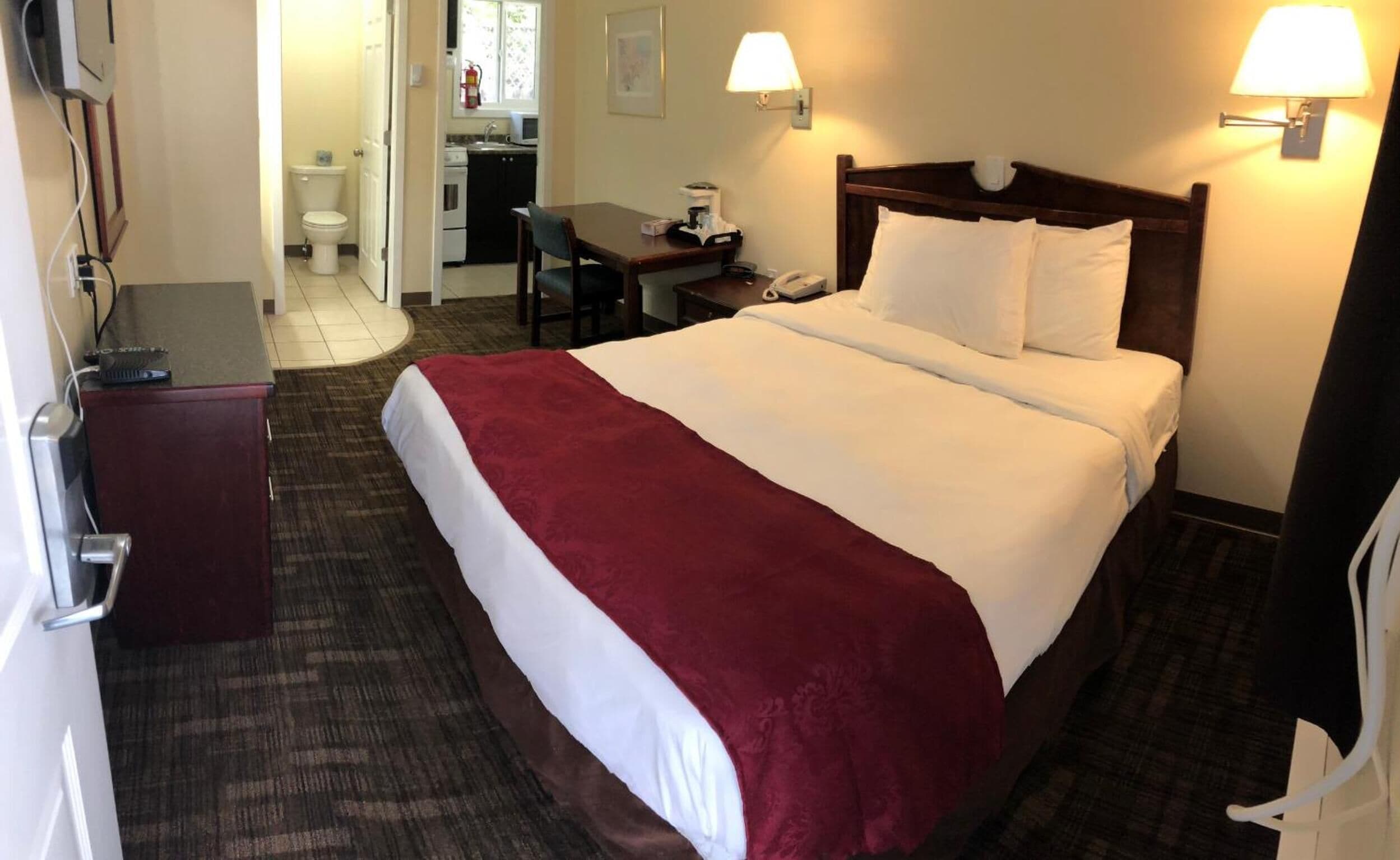 Una habitación de hotel con una cama grande, un escritorio, una silla, un teléfono y una kitchenette pequeña.