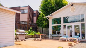 A backyard with a wooden deck, a barbecue grill, a table with chairs, and two lounge chairs. - Kings Motor Inn (Kamloops)