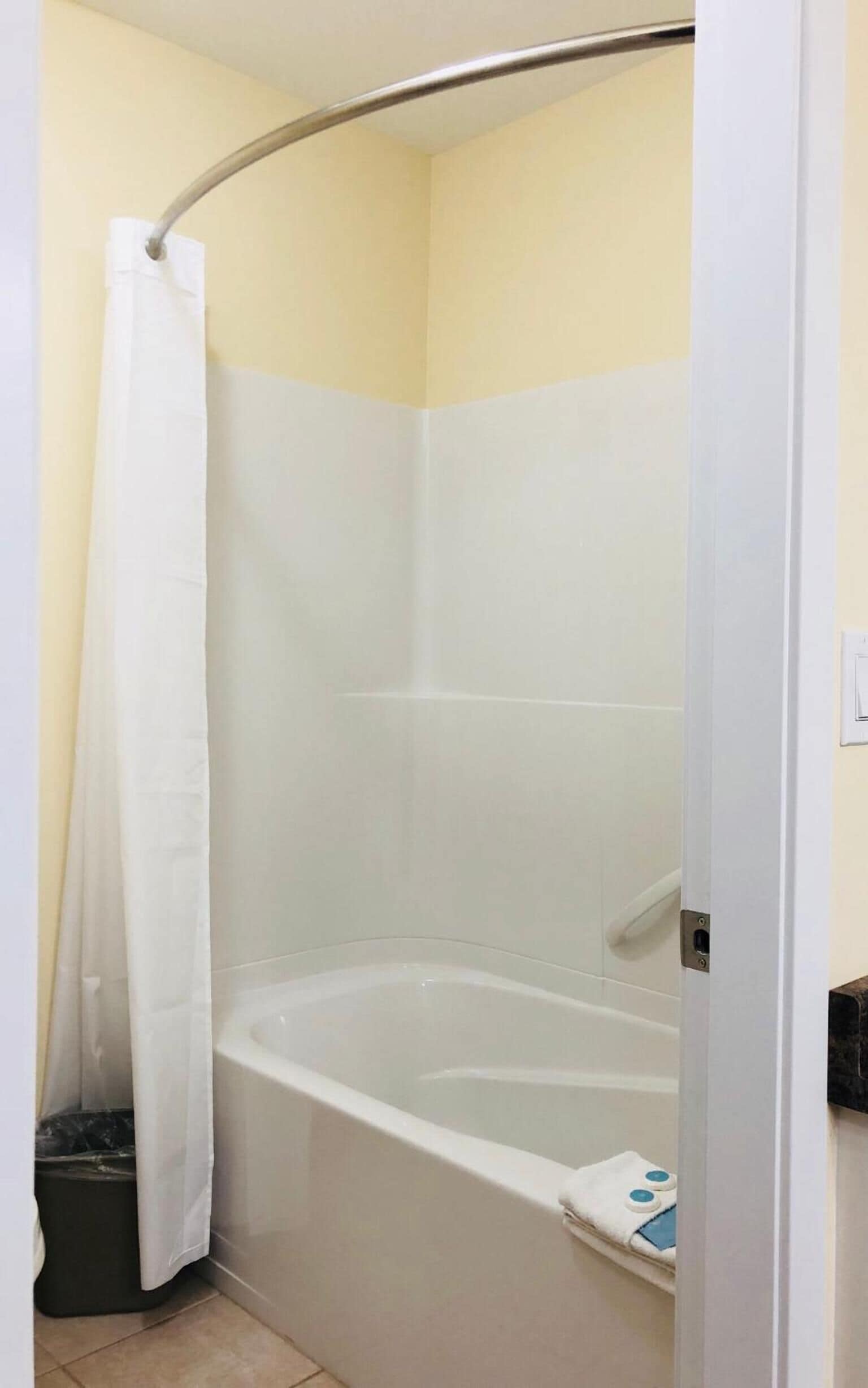 A small, enclosed shower area with a white bathtub, a shower curtain, and a tiled wall.