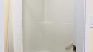 A small, enclosed shower area with a white bathtub, a shower curtain, and a tiled wall.