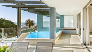 A modern outdoor pool area with a clear view of the sea, a pergola structure, and a glass door leading to a room. - Blue Views Penthouse Beachfront Apartments (Cape Town)