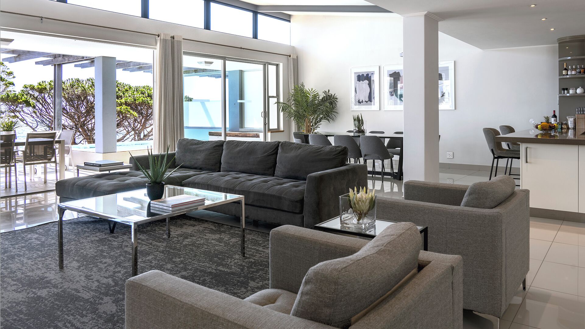 A modern living room with a grey sofa, a glass coffee table, and a dining area with a bar.
