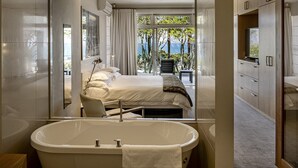 A modern bedroom with a large window, a bathtub, and a view of the outdoors. - Blue Views Penthouse Beachfront Apartments (Cape Town)