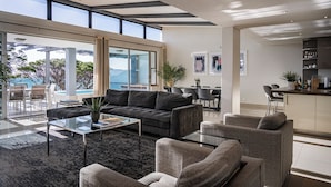 A modern living room with a dark grey sofa, a glass coffee table, and a view of the outdoors. - Blue Views Penthouse Beachfront Apartments (Cape Town)