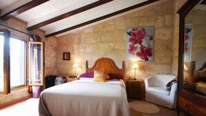 A bedroom with a bed, a chair, a nightstand, a lamp, and a painting on the wall. - Fínca Líbertad (Campos)