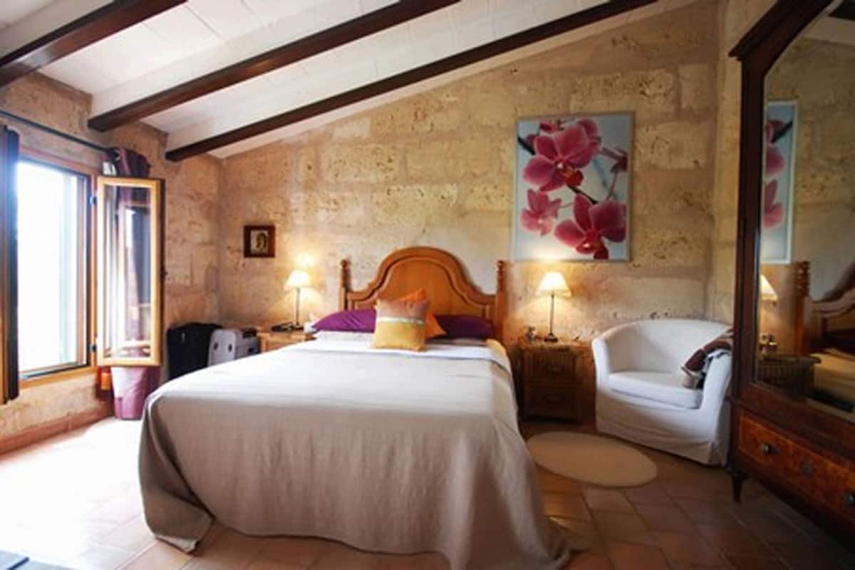 A bedroom with a bed, a chair, a nightstand, a lamp, and a painting on the wall.
