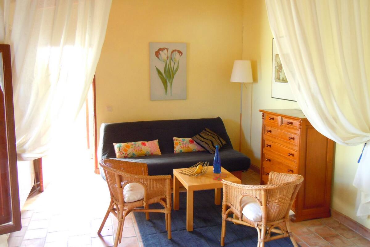 A living room with a sofa, two wicker chairs, a small table, a lamp, and a dresser.