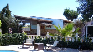 A pool area with lounge chairs, a thatched-roof structure, and a house with stone walls and a white facade. - Fínca Líbertad (Campos)