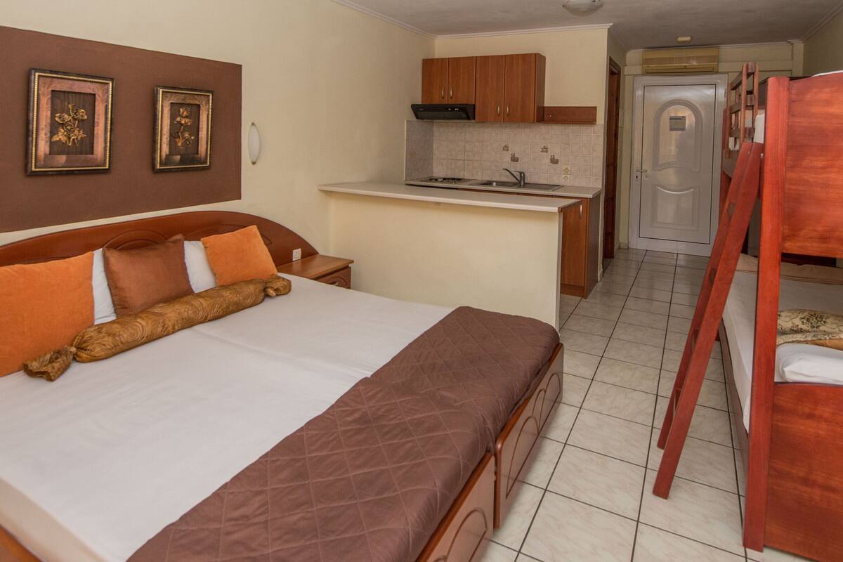 A hotel room with a bed, a bunk bed, a kitchenette, and a bathroom.