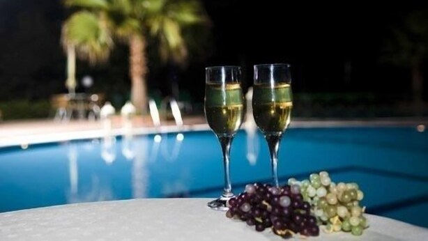 Two glasses of white wine and a plate of grapes by a poolside at night. - Damia Hotel (Corfu)