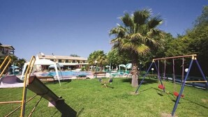 A grassy area with a swing set, a slide, and a pool in the background. - Damia Hotel (Corfu)