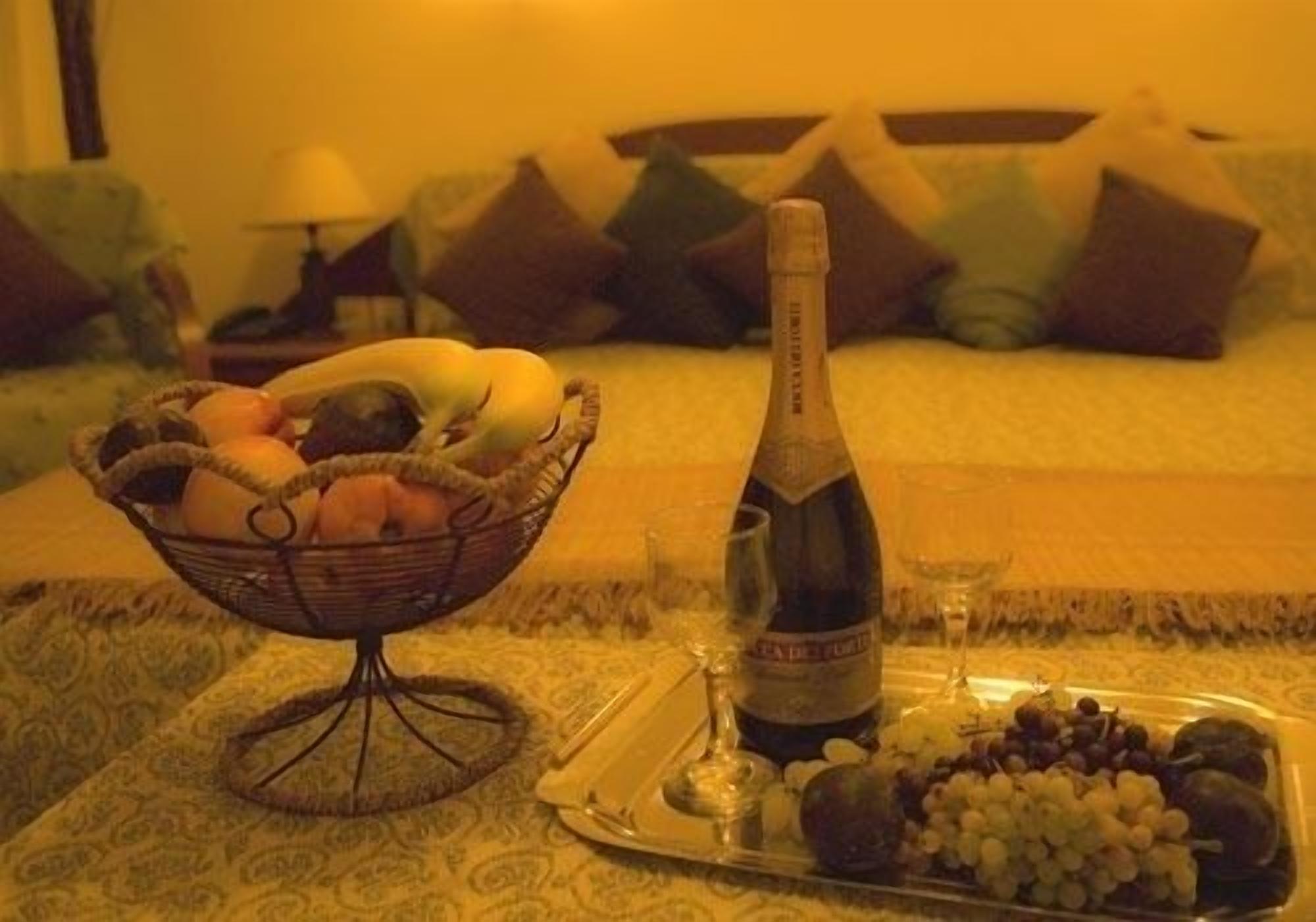 Eetgedeelte met een fruitmand, een fles champagne en een schaal druiven op een bed.