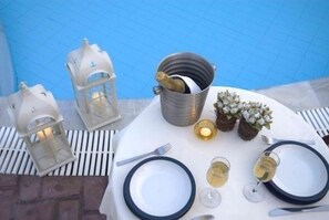 A table set for two with white plates, cutlery, and glasses of white wine, accompanied by a metal bucket and two lanterns. - Damia Hotel (Corfu)