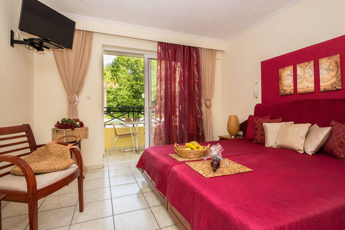 A hotel room with a bed, a chair, a television, and a balcony with a table and chairs.