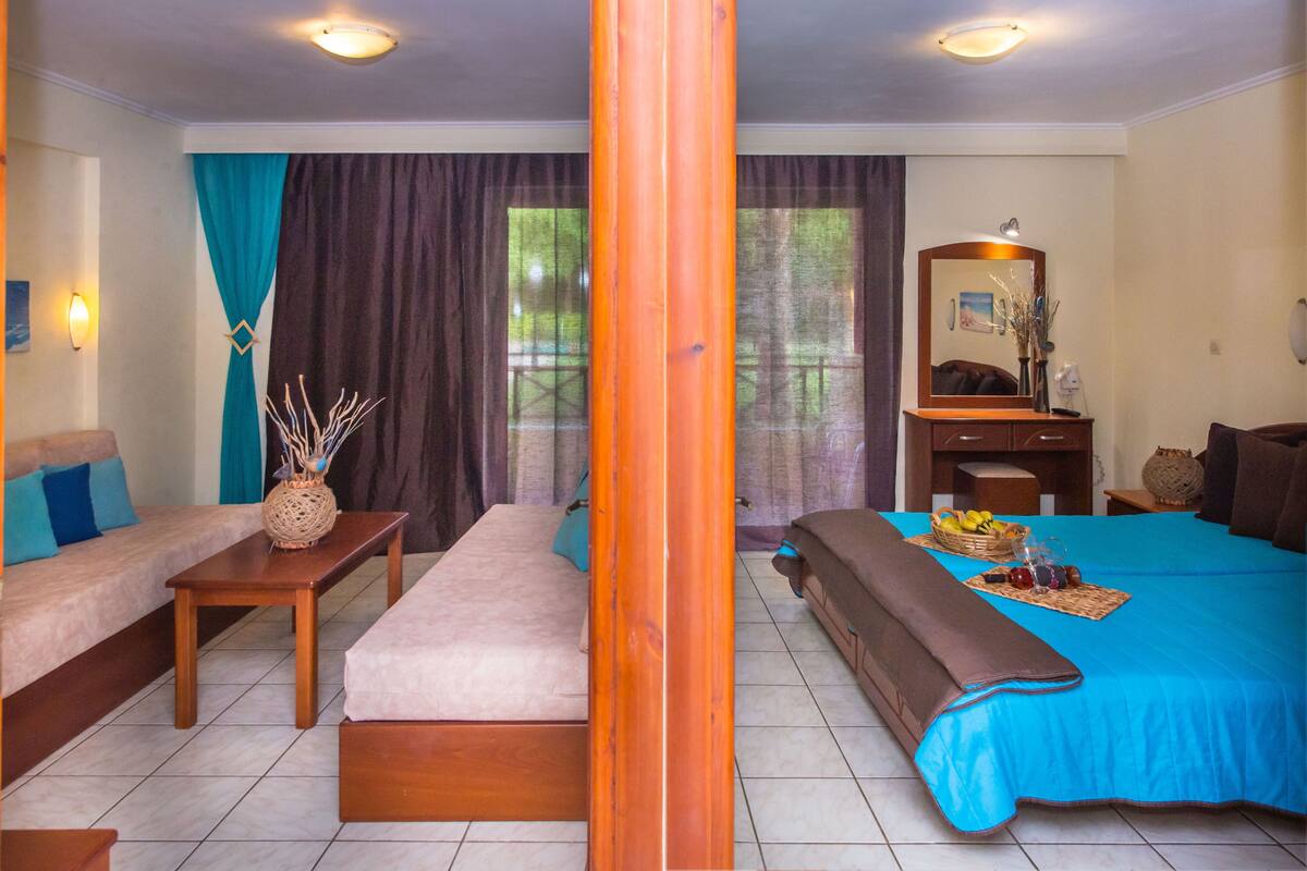 A hotel room with a sofa, a bed, a small table with a vase, and a mirror.