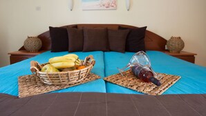 A bed with a blue bedspread, a basket of fruit, and a wine bottle on a woven placemat. - Damia Hotel (Corfu)