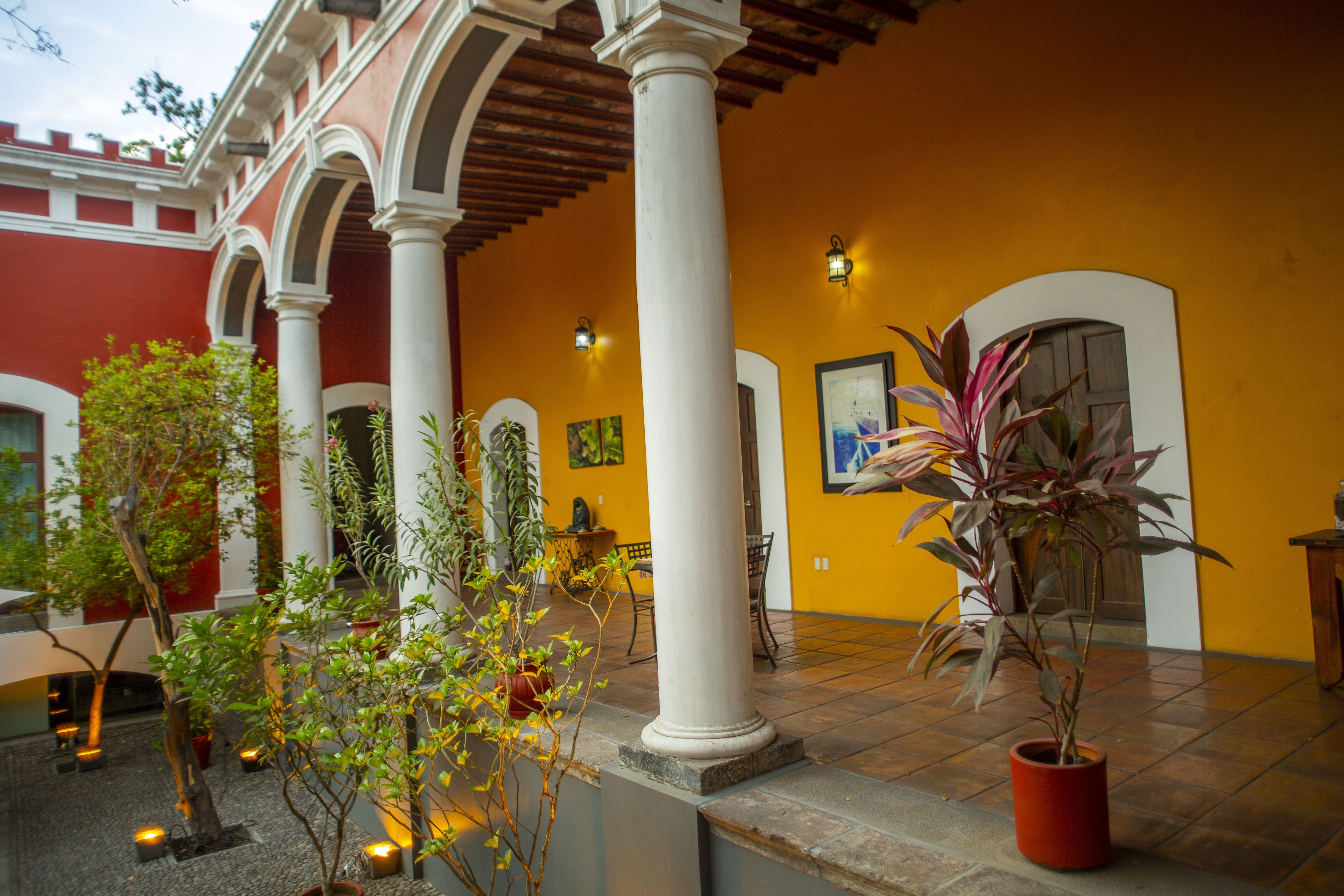 A courtyard with columns, potted plants, and a yellow wall.