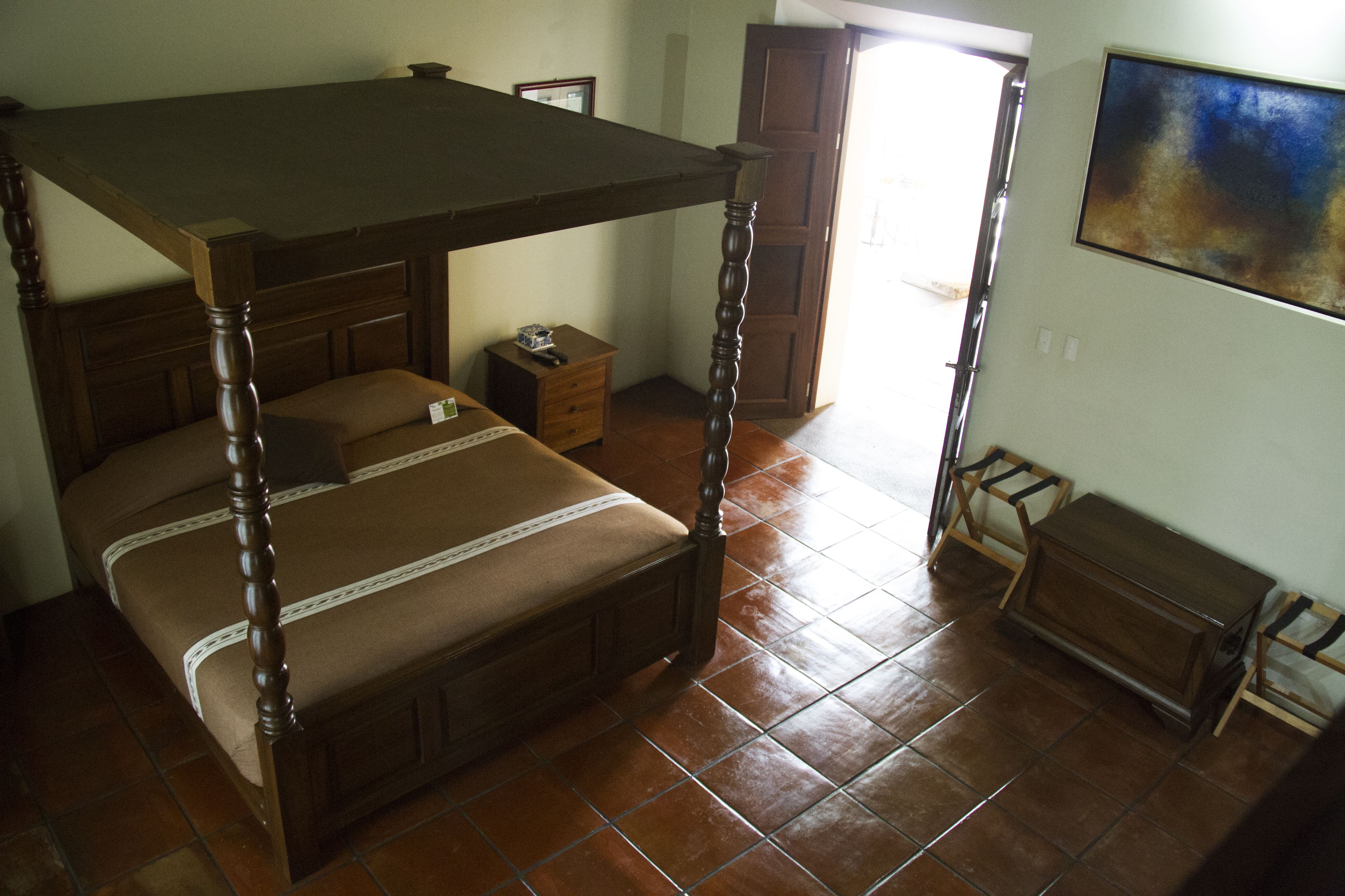 A bedroom with a four-poster bed, a wooden dresser, and a small table.