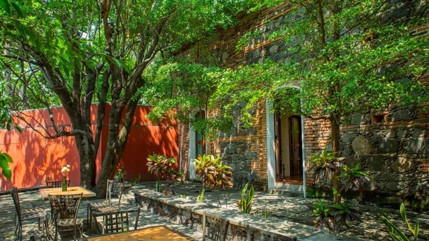 An outdoor patio with tables and chairs, surrounded by stone walls and greenery. - Hotel Boutique Hacienda del Gobernador (Colima)