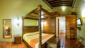 A four-poster bed with a wooden headboard, a nightstand, a mirror, and a television on a stand. - Hotel Boutique Hacienda del Gobernador (Colima)